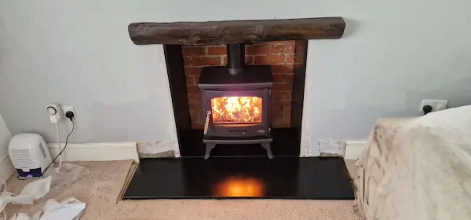 Wood-burning stove lit in the brick opening with rustic timber mantel and black hearth